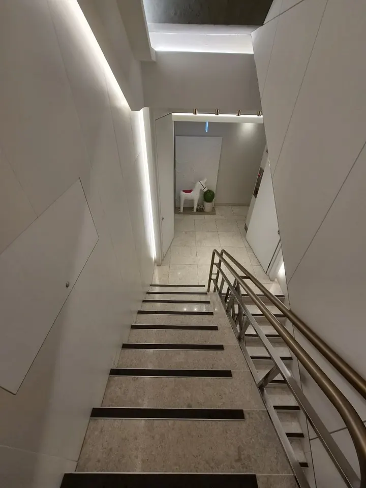 간접 조명이 비추는 흰 벽을 따라 아래층으로 내려가는 계단